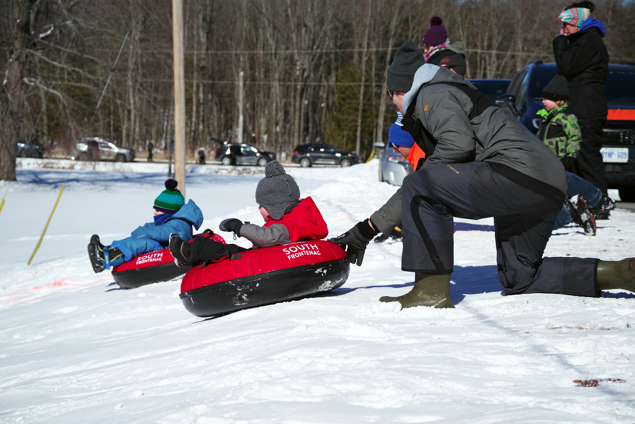 A parent pushes their child down a snowy hill in an inflatable tube